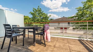 Un balcon avec une table et des chaises, une vue sur un immeuble et une clôture.