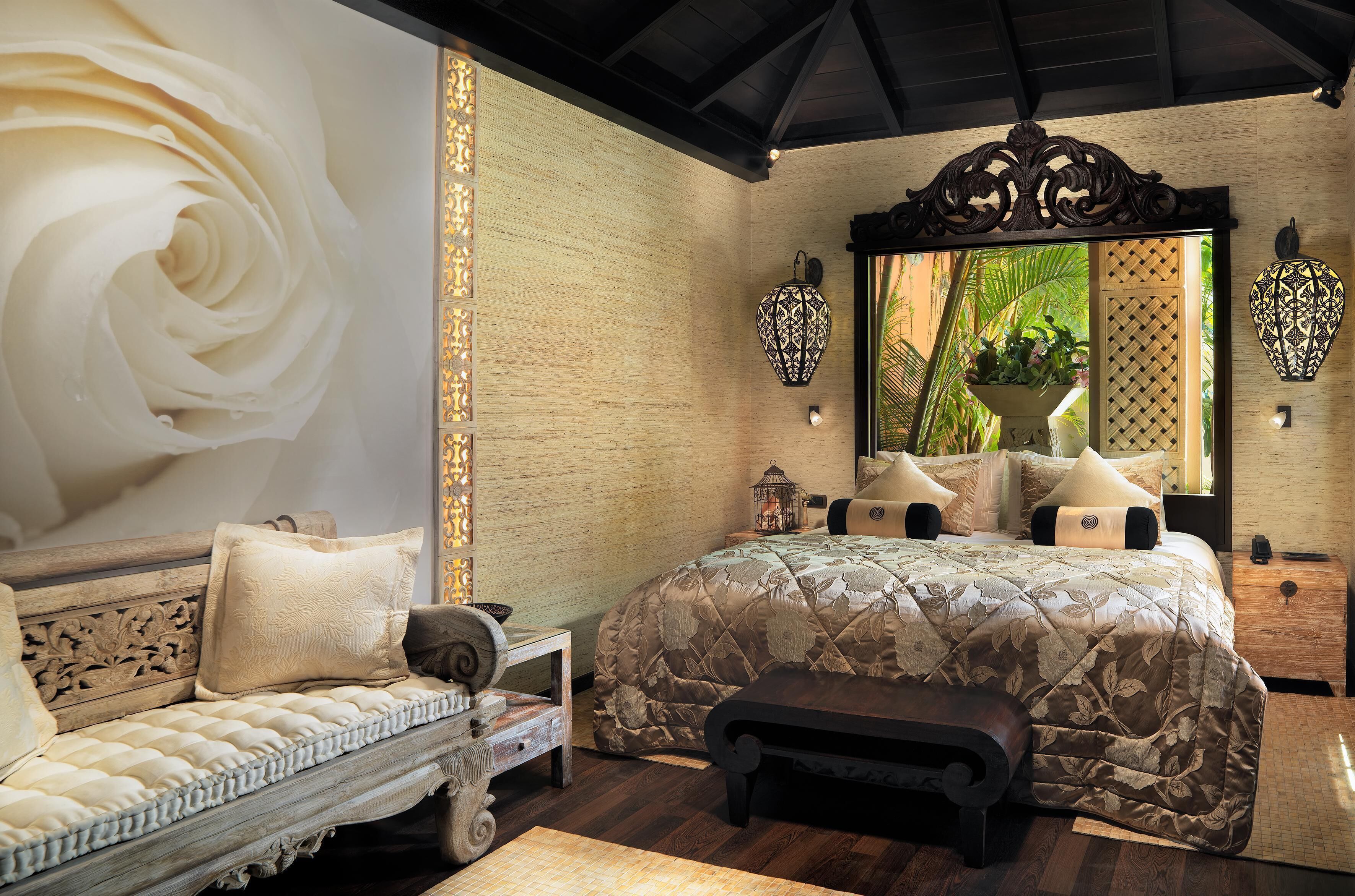 A bedroom with a large bed, a sofa, a bench, and a decorative wall with a large floral design.