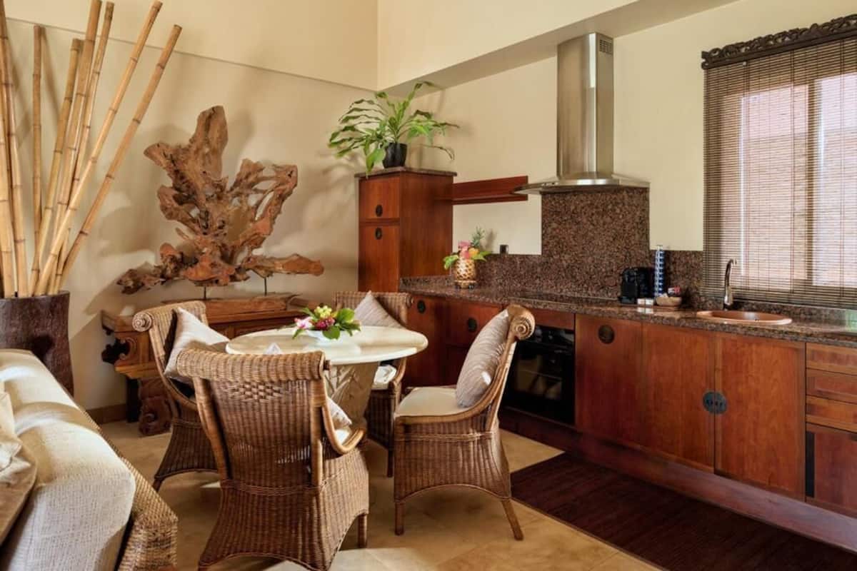 A kitchen with a round table, wicker chairs, a granite countertop, wooden cabinets, a stainless steel range hood, and a large decorative plant.