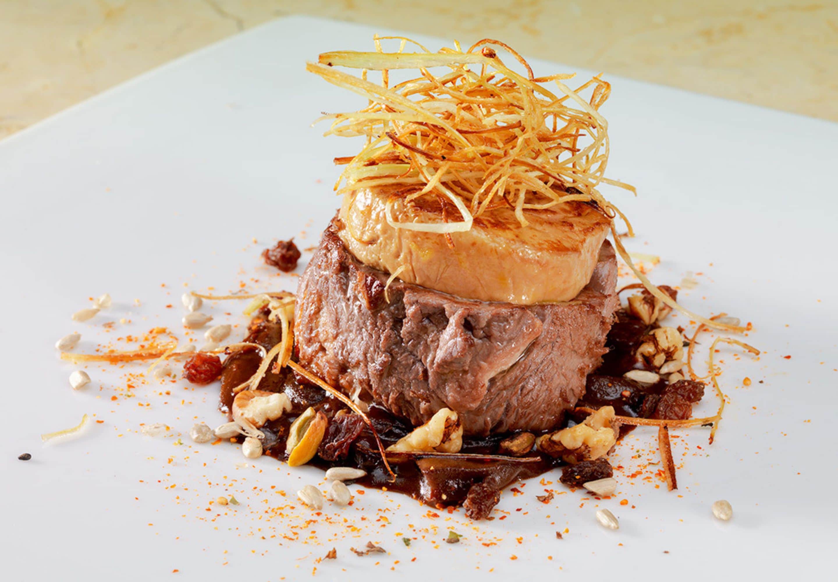 Un plat composé d’une portion de viande centrale, agrémentée d’éléments émincés et entourée de différentes graines et épices.