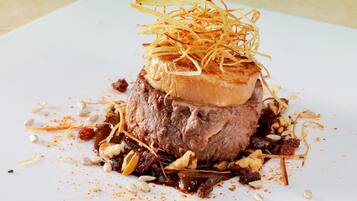 Un plat composé d’une portion de viande centrale, agrémentée d’éléments émincés et entourée de différentes graines et épices.