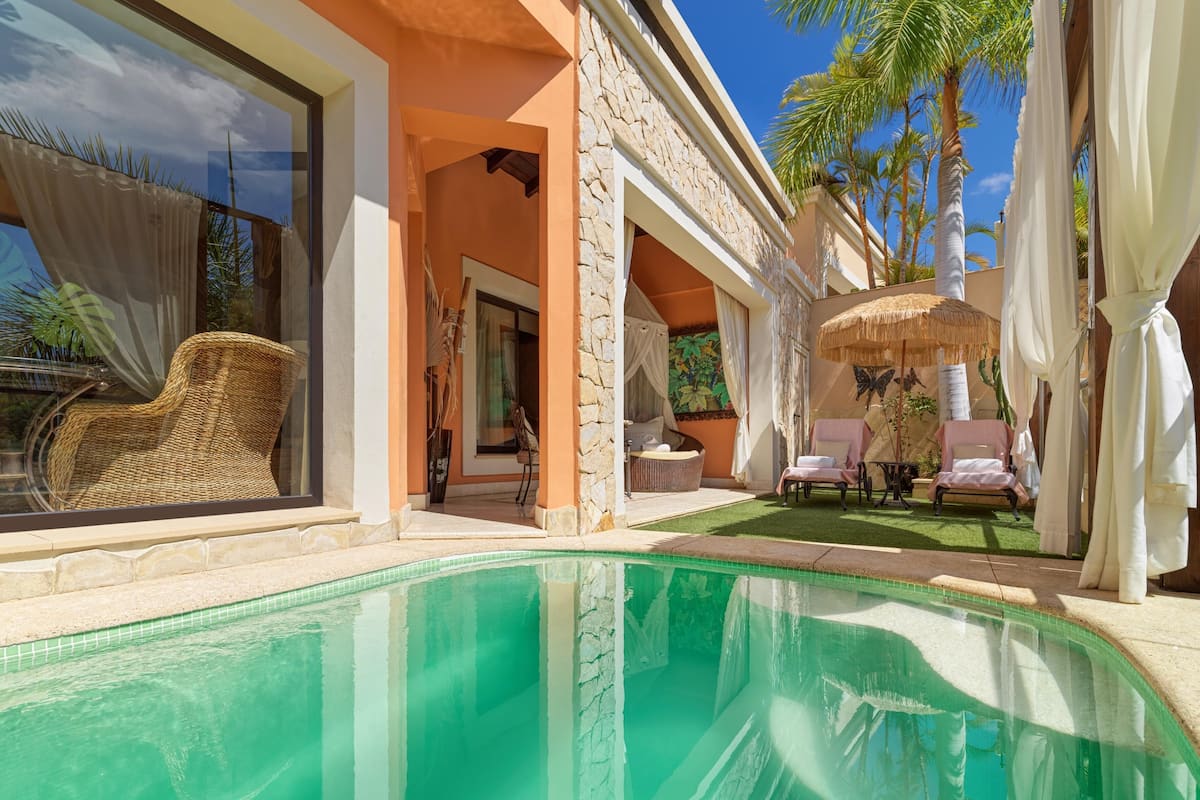 A poolside area with a clear view of the pool, lounge chairs, and a thatched umbrella.