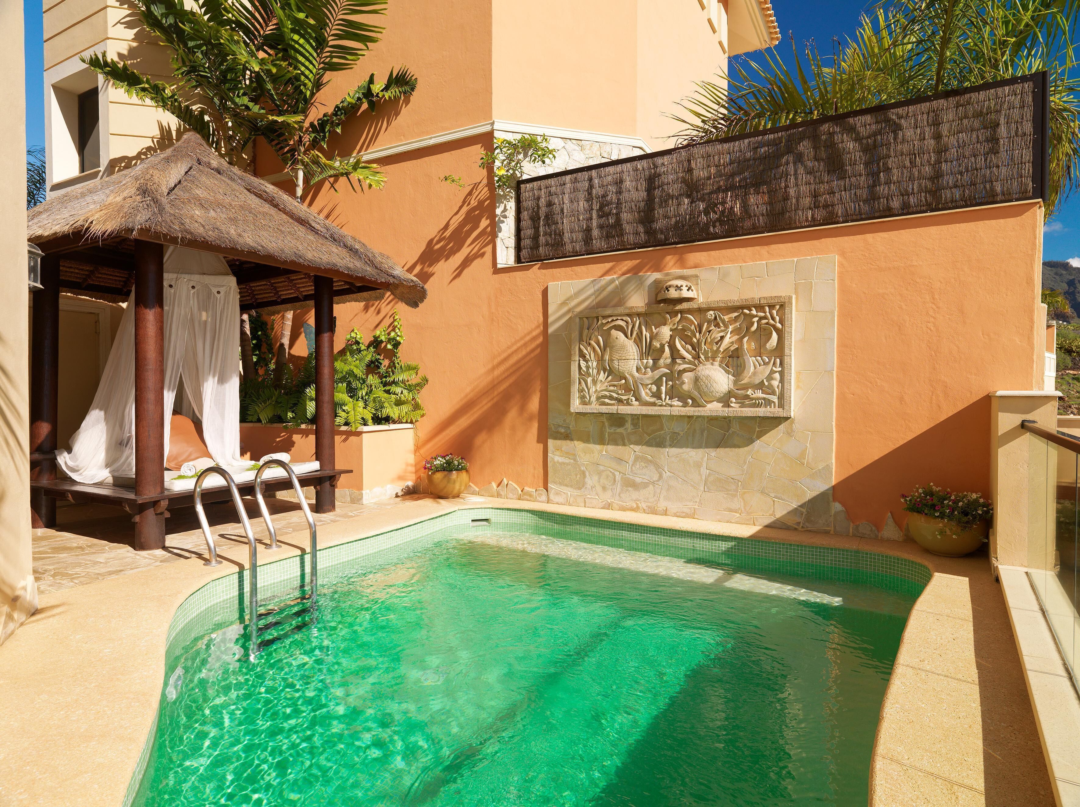 Una piscina con un paraguas de paja y una pared de piedra con un relieve escultórico.