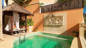 Una piscina con un paraguas de paja y una pared de piedra con un relieve escultórico.
