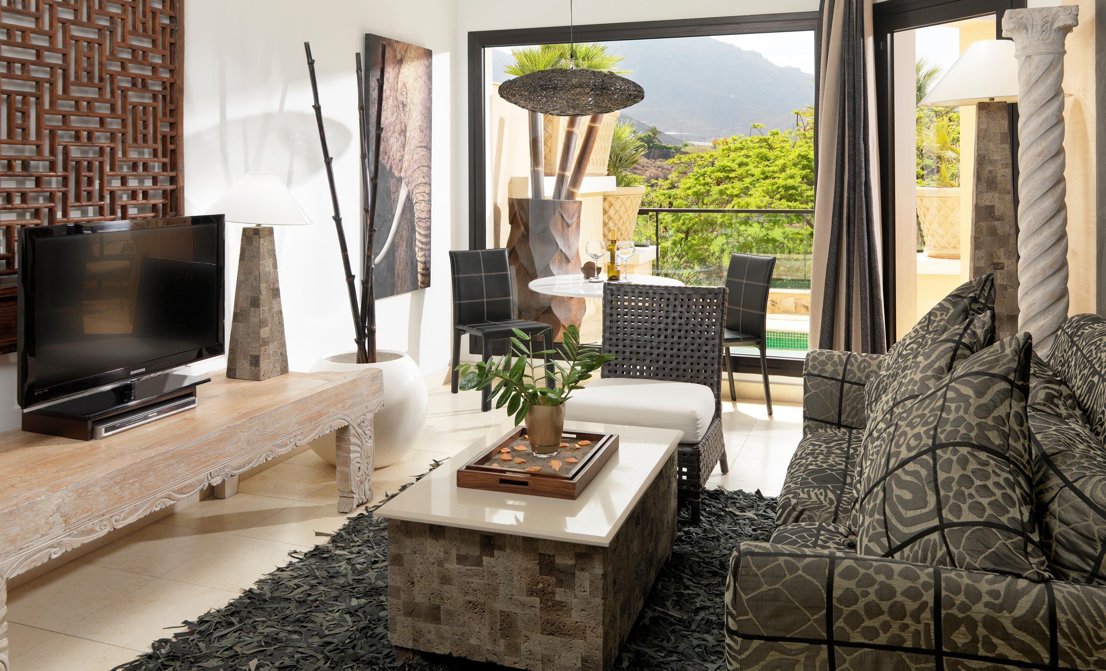 Sala de estar com televisão, sofá, mesa de centro e vista para o exterior.