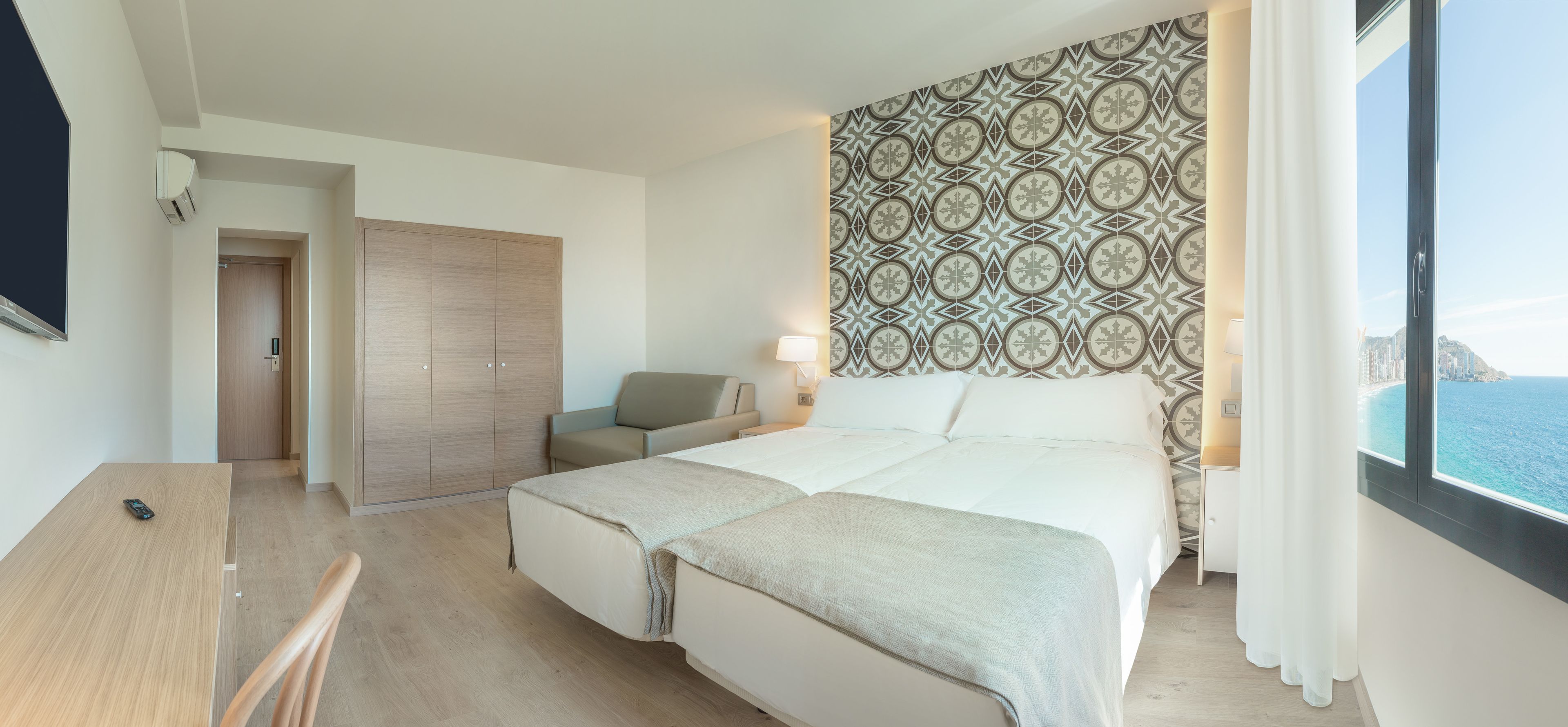 Une chambre d’hôtel avec un lit, un bureau, une chaise, une armoire et une vue sur la mer.
