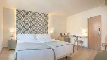 A hotel room with two beds, a desk, a chair, a TV, and a patterned wall.