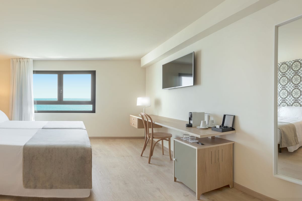 A hotel room with a bed, a desk, a chair, a TV, and a window with a view.