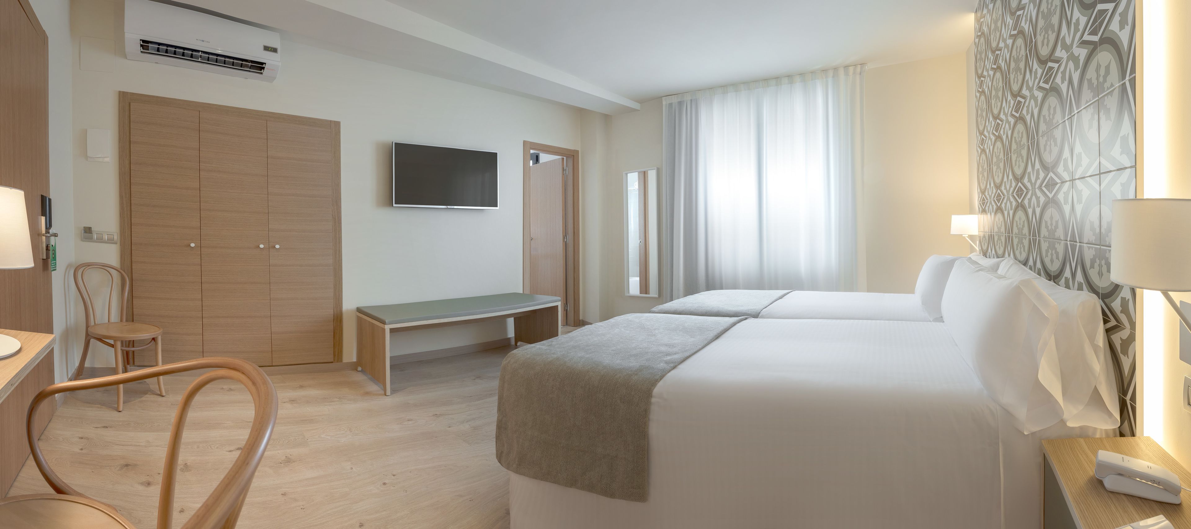 Een hotelkamer met twee bedden, een bureau, een stoel, een televisie en een groot, patroonbehang.
