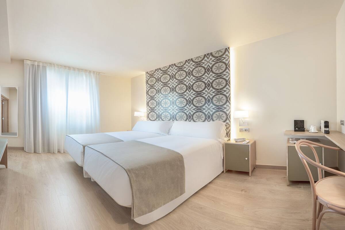A hotel room with a large bed, bedside tables, a desk, a chair, and a TV.