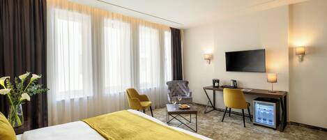 A hotel room with a bed, a desk, a chair, a television, and a minibar.
