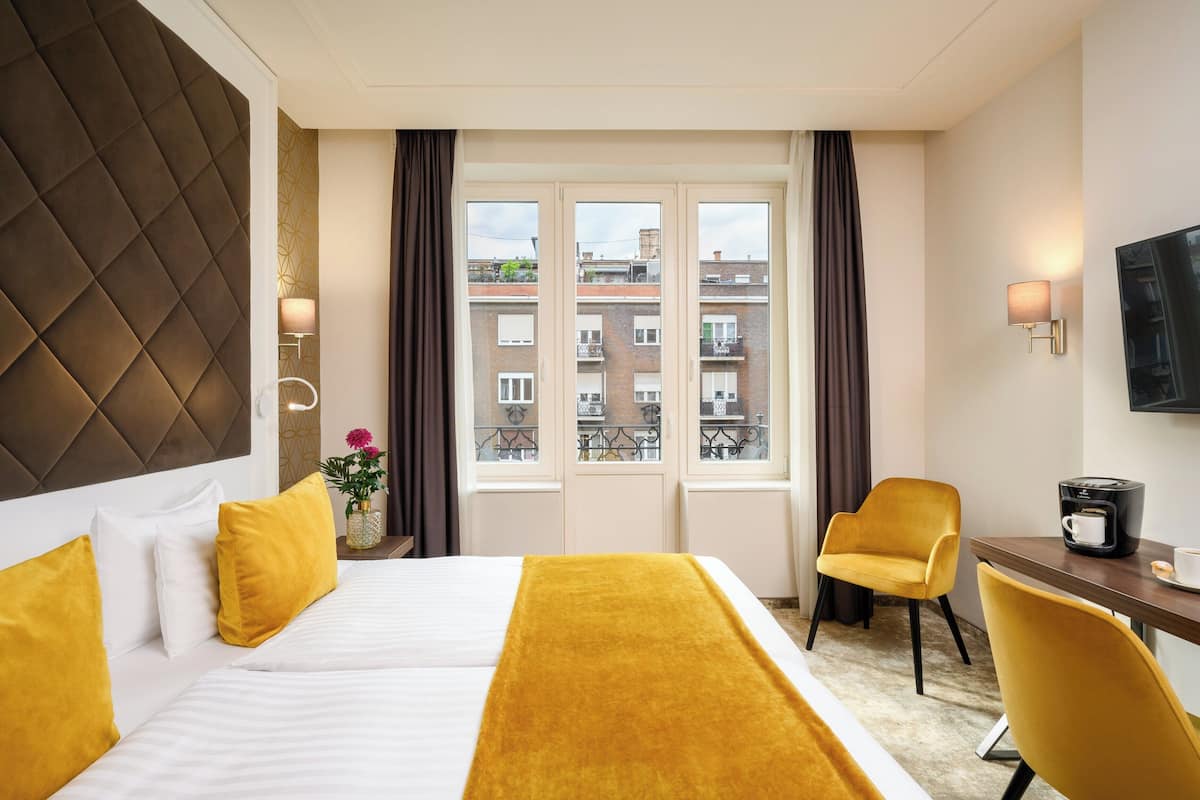 A hotel room with a bed, a desk, a chair, a coffee maker, and a TV.