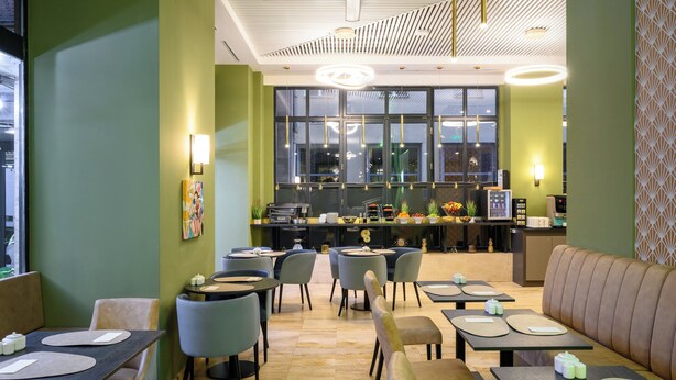 Un restaurante moderno con una paleta de colores verde y beige, que cuenta con una zona de bar, diferentes disposiciones de asientos y un amplio ventanal con vistas a la ciudad.