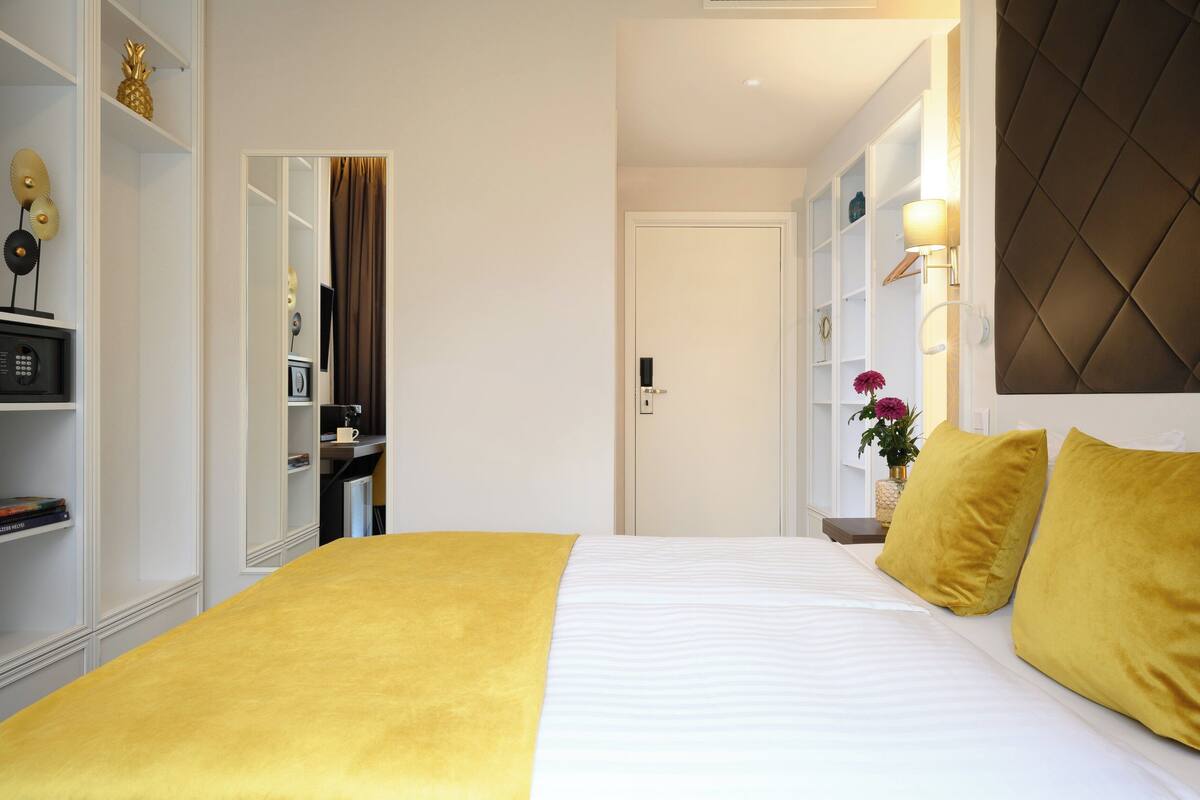 A hotel room with a bed, a wardrobe, a mirror, and a nightstand with a lamp.
