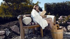Una persona sentada en un banco de madera al aire libre, leyendo un libro, rodeada de rocas y vegetación.