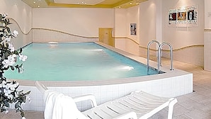 A swimming pool with a tiled deck, lounge chairs, and a ceiling with recessed lighting. - Alpine Wellfit Hotel Eagles-Astoria (Innsbruck)