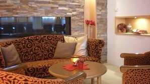 A cozy seating area with patterned sofas and a small round table, featuring a stone wall and a window with a view. - Alpine Wellfit Hotel Eagles-Astoria (Innsbruck)