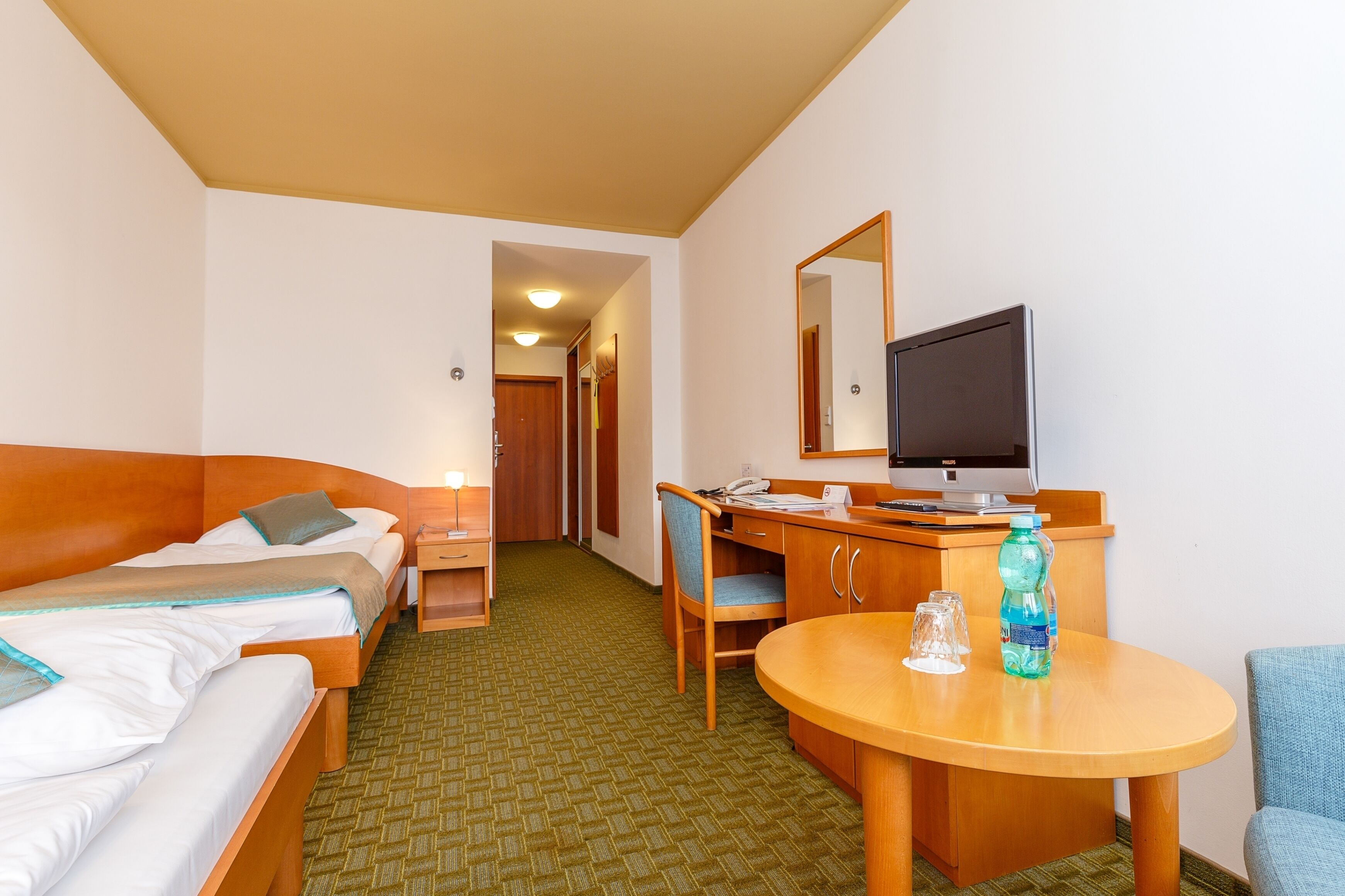 Een hotelkamer met twee bedden, een bureau met computer, een stoel, een ronde tafel en een televisie.