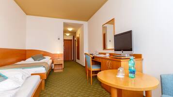 Een hotelkamer met twee bedden, een bureau met computer, een stoel, een ronde tafel en een televisie.