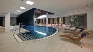 Una piscina interior con sillones de descanso y una pared de vidrio.