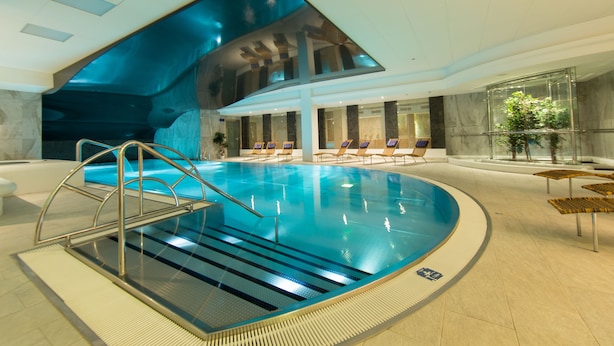 Una piscina interior con diseño moderno, que incluye techo de vidrio y sillones de descanso alrededor de la zona de la piscina.