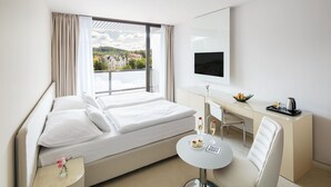 Una habitación de hotel con cama, escritorio, silla, una mesita con una copa de vino y televisión en la pared.