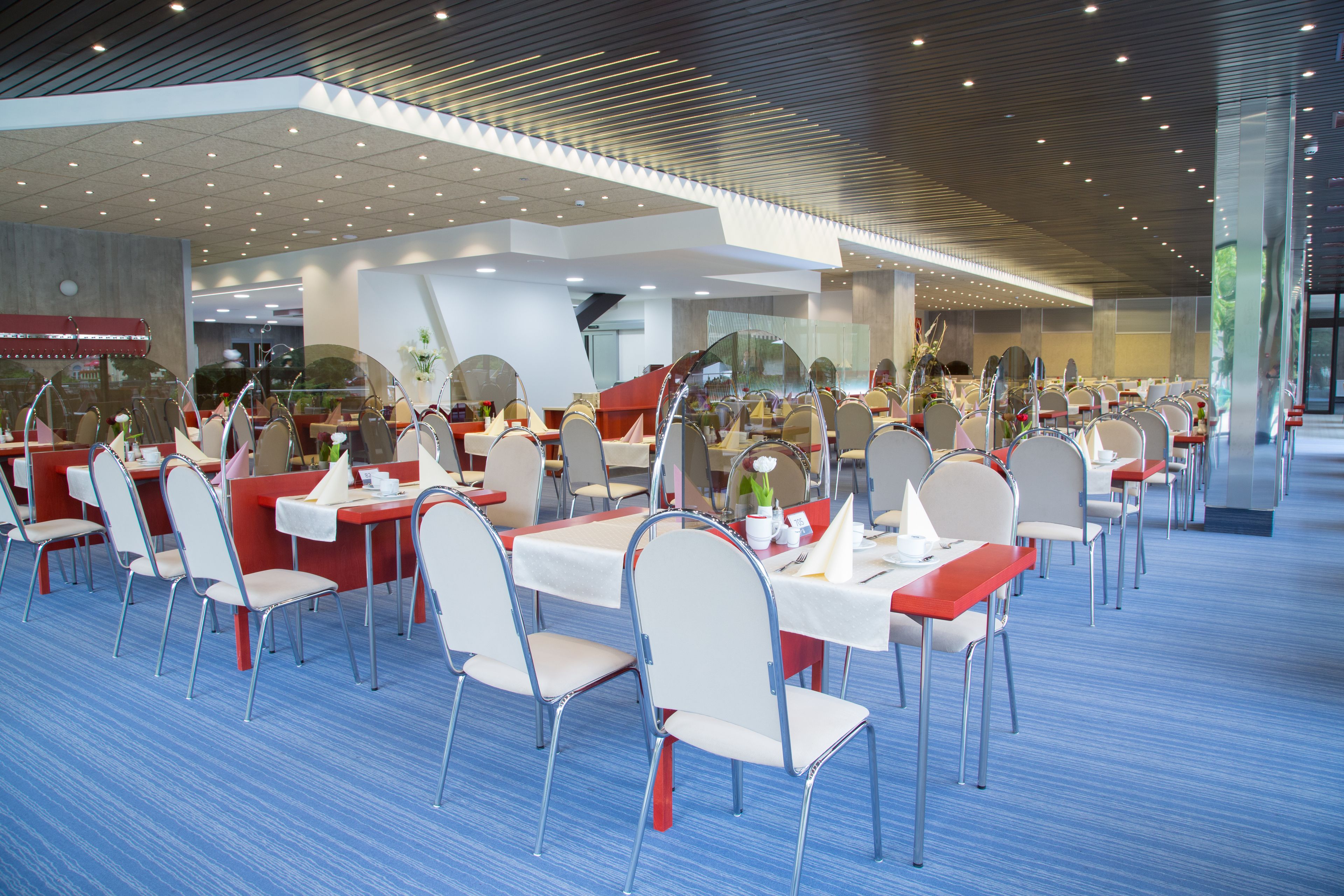 A modern dining area with multiple tables and chairs, featuring a blue carpet and a contemporary ceiling design.