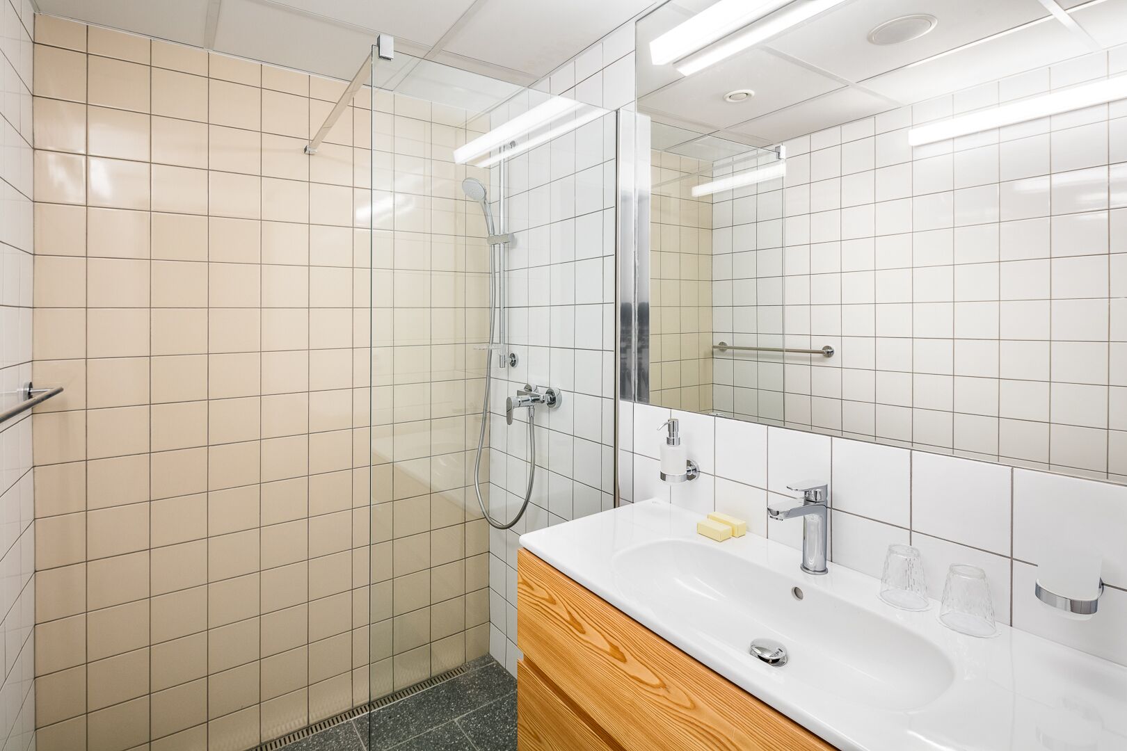 A modern bathroom with a glass-enclosed shower, a white sink with a wooden vanity, and a large mirror.