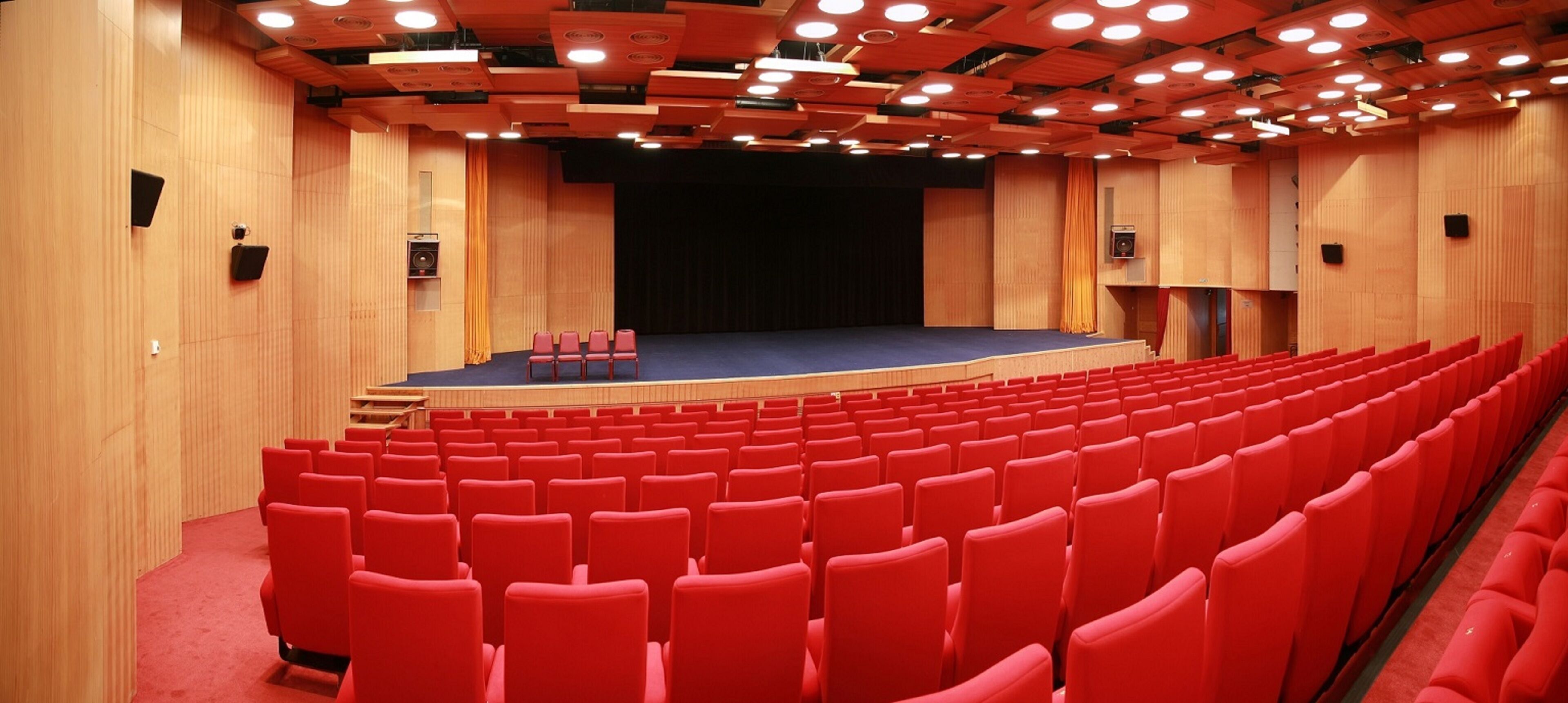 An auditorium with rows of red seats, a stage, and wooden paneling.