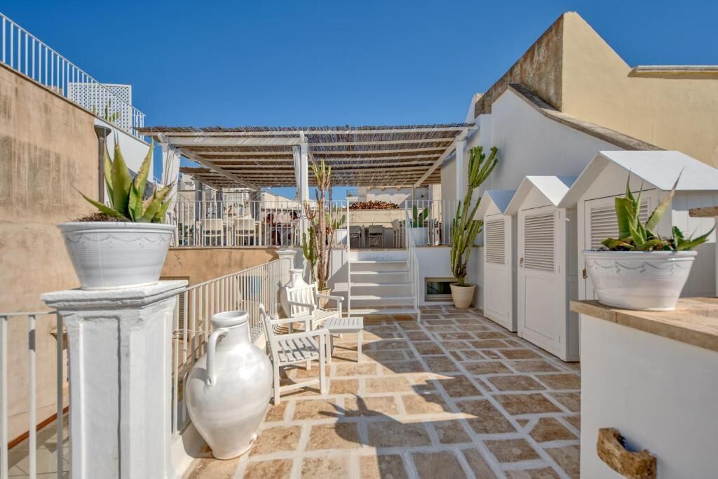 A rooftop terrace with white furniture, potted plants, and a pergola.
