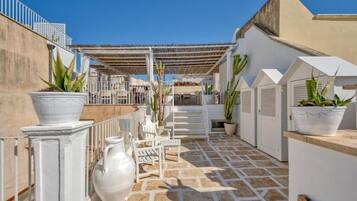 A rooftop terrace with white furniture, potted plants, and a pergola.