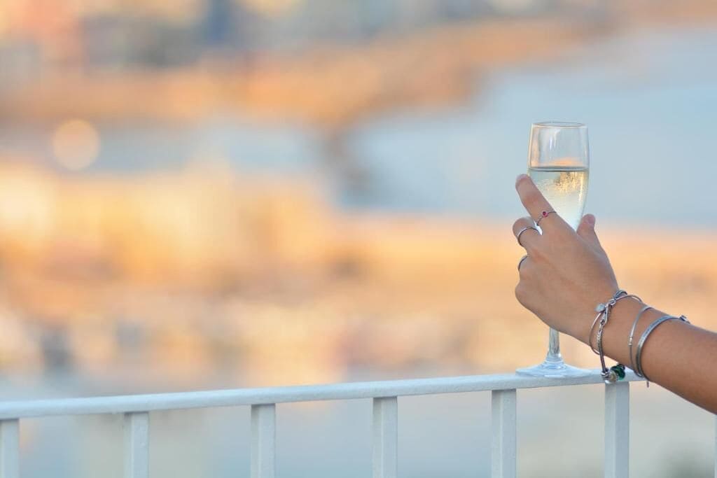 A hand holding a glass of white wine against a blurred background.