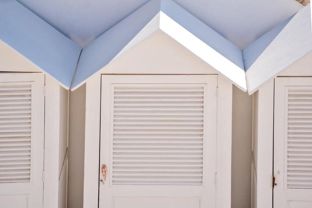 A corner of a building with two white doors with horizontal blinds, and a blue-painted ceiling.