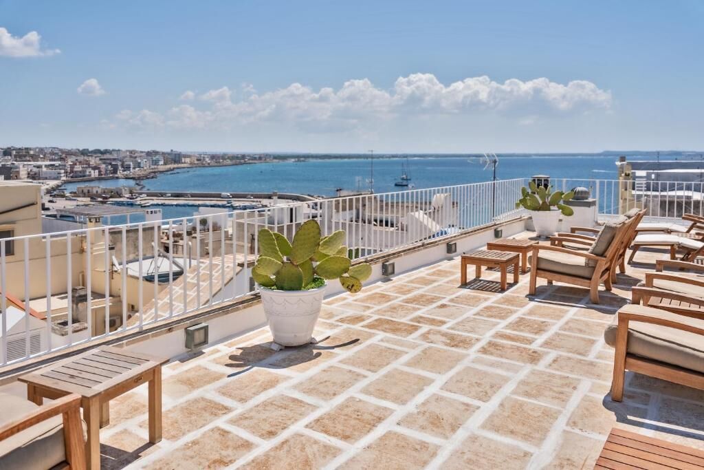 Eine Dachterrasse mit Blick auf das Meer, üppigen Pflanzen und Holzliegen.