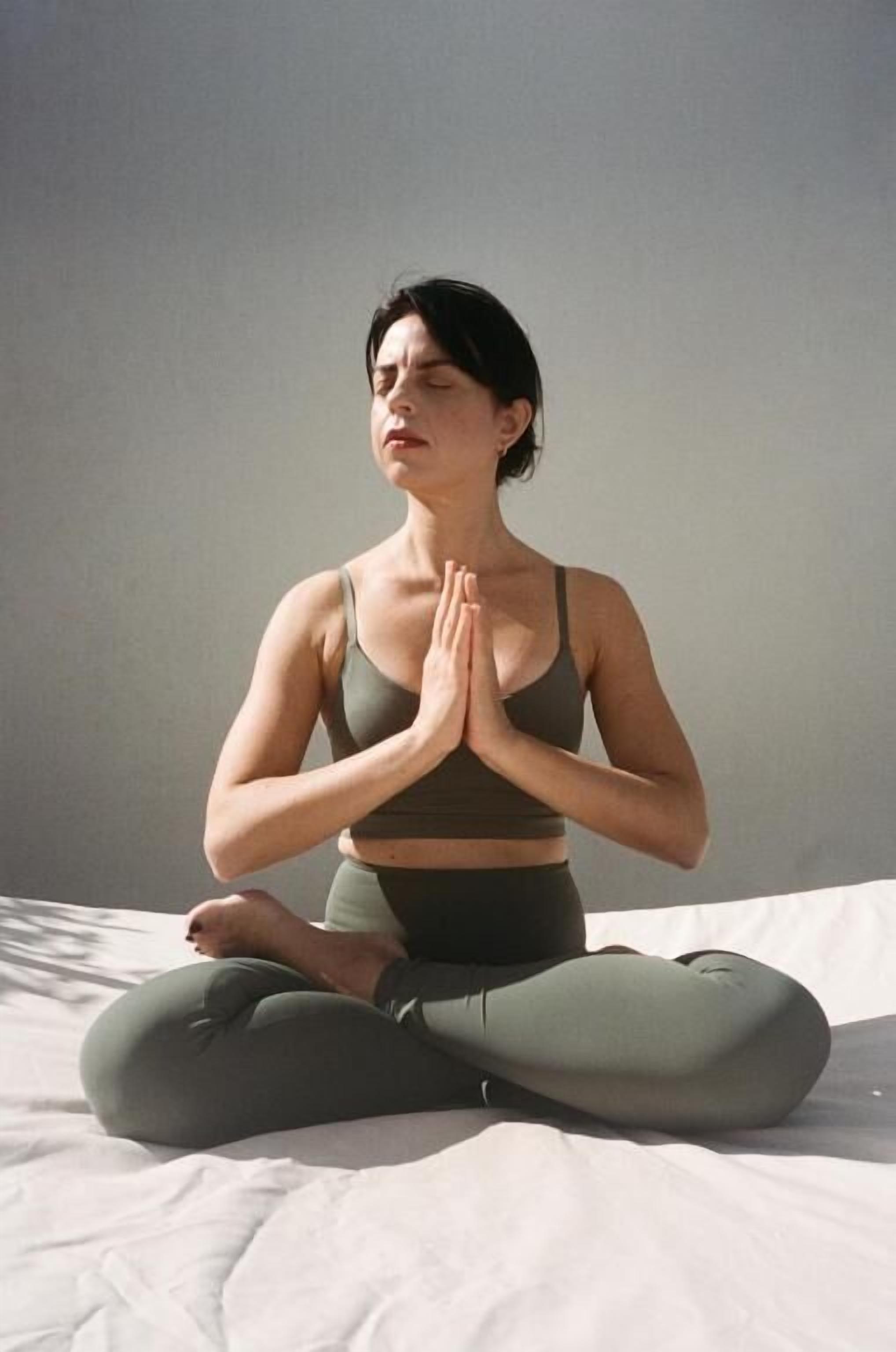 A person sitting cross-legged on a bed in a room with a plain wall.