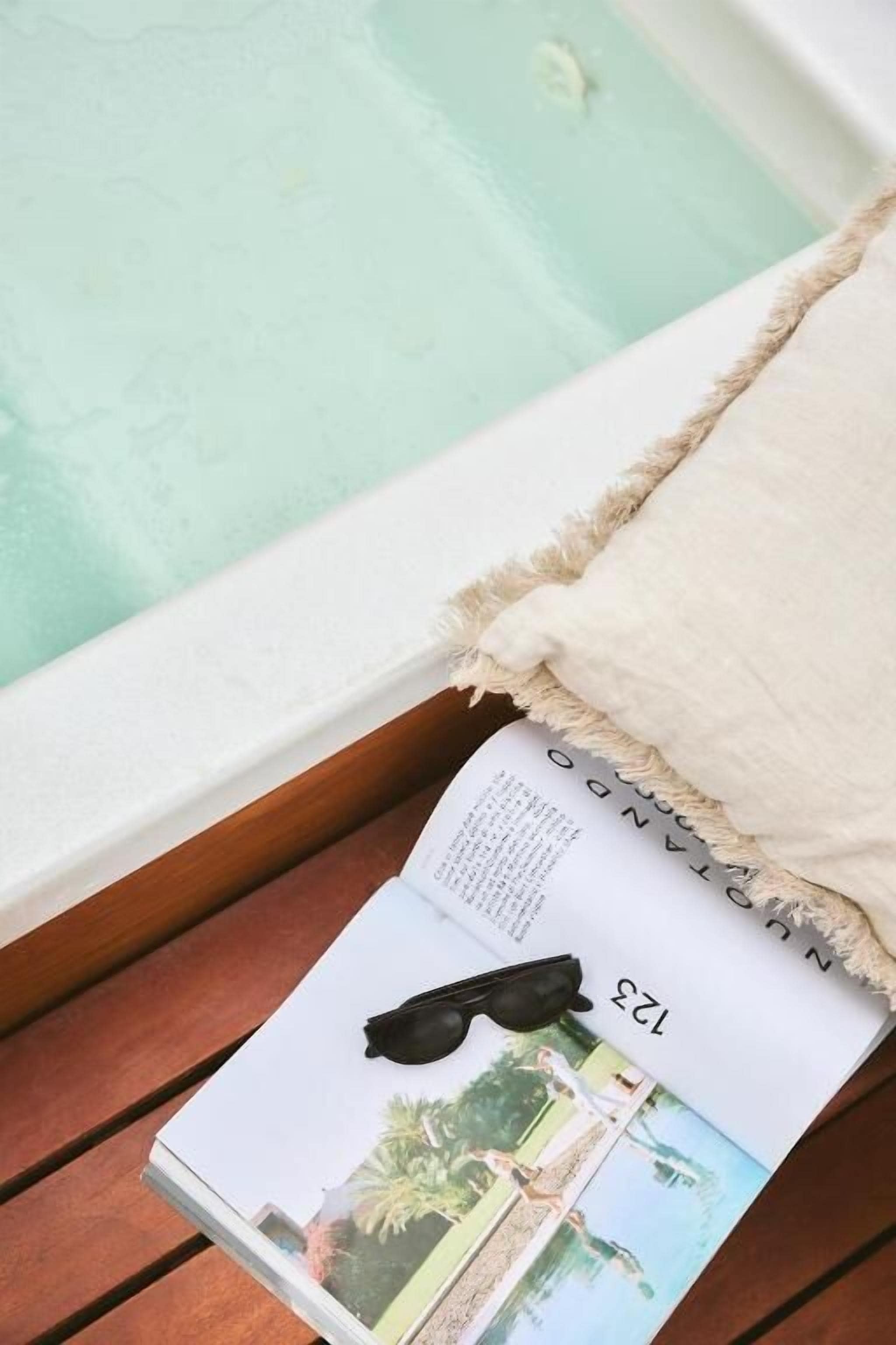 Eine Zeitschrift auf einer Holzfläche nahe einer Badewanne mit einem weißen Handtuch.