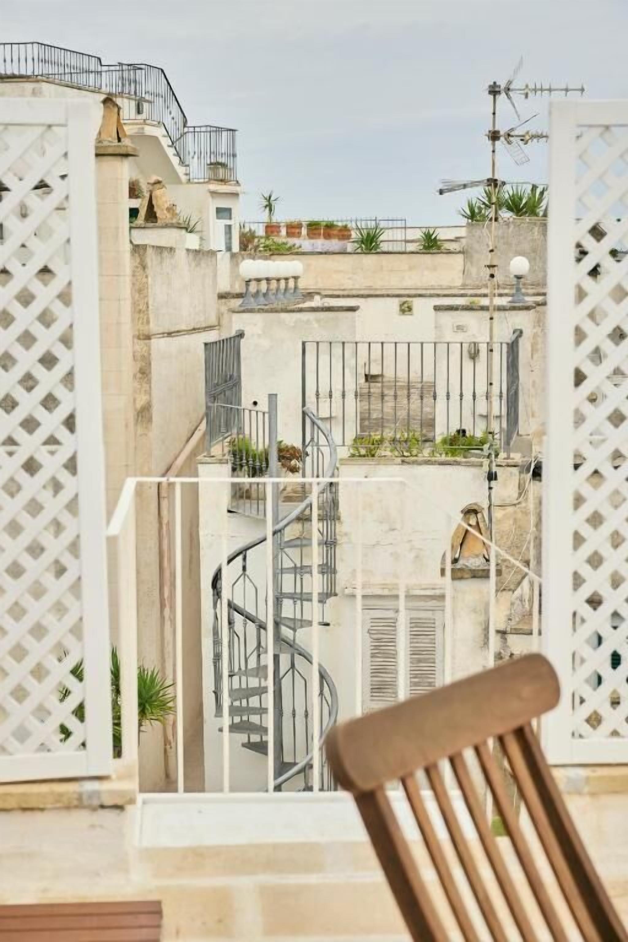 A balcony with a view of a cityscape, featuring a spiral staircase and a wooden chair.