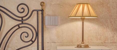A bed with a metal headboard, a bedside table with a lamp, and a wall-mounted light switch.