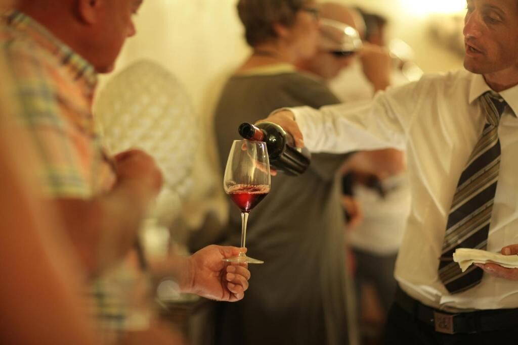A person pouring wine into a glass held by another individual.