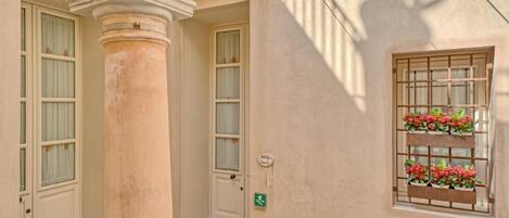 Un edificio con una columna, una puerta y una ventana adornada con macetas de flores.