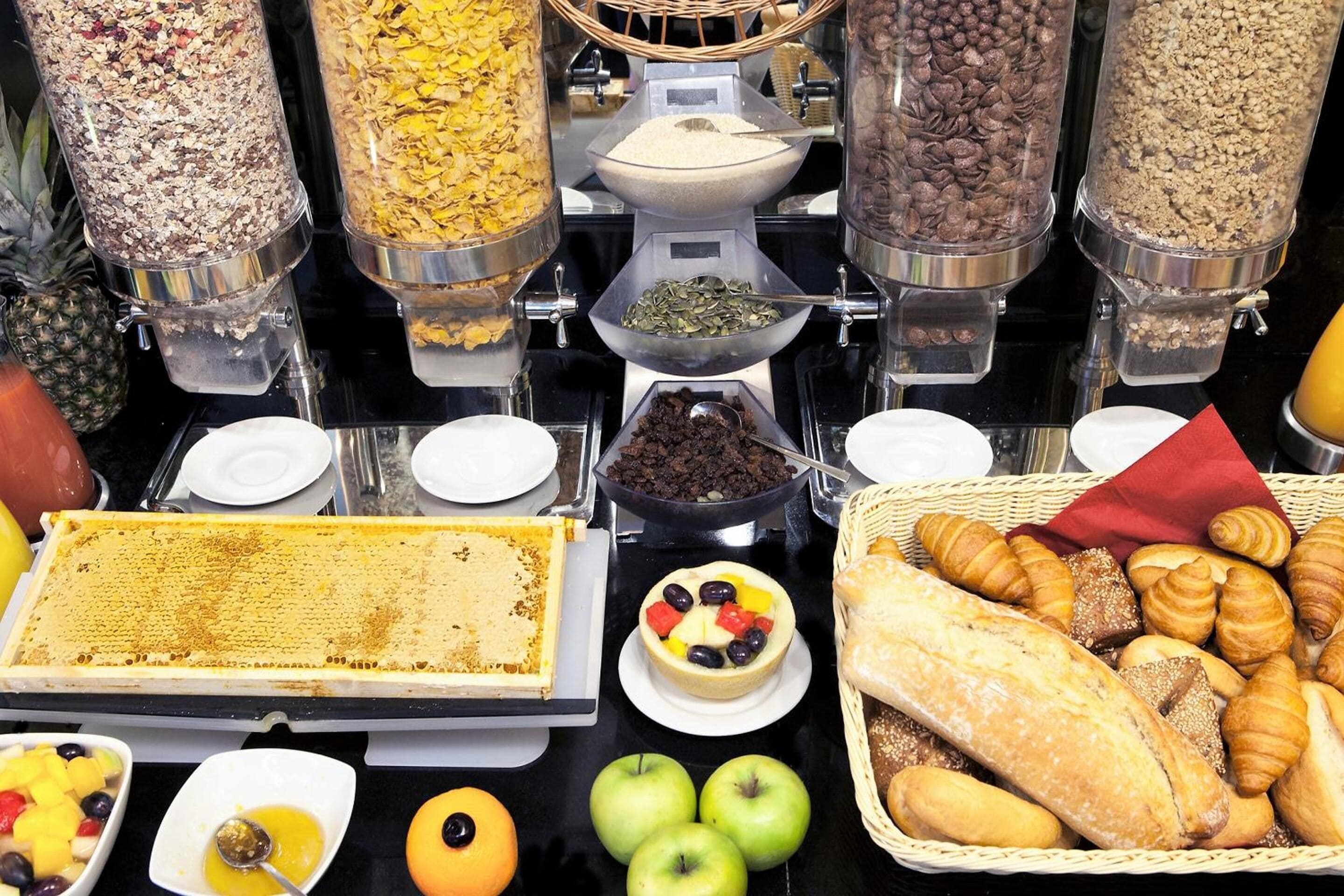 Un bufé con distintos alimentos, entre ellos pasteles, frutas y un recipiente rectangular grande.
