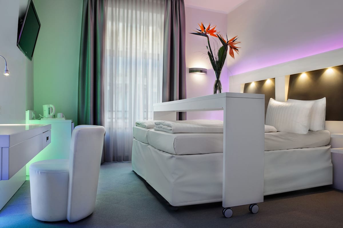 Een moderne hotelkamer met een stapelbed, een bureau met stoel, een nachtkastje en een vaas met bloemen.
