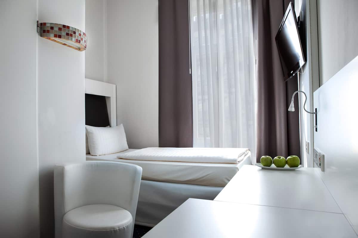 Een moderne hotelkamer met een bed, een wit bureau, een stoel en een wandgemonteerde flatscreen televisie.