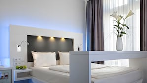 Een moderne hotelkamer met een bed, nachtkastje en een vaas met bloemen.