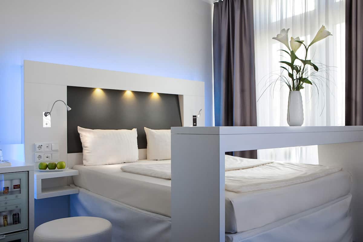 Een moderne hotelkamer met een bed, nachtkastje en een vaas met bloemen.
