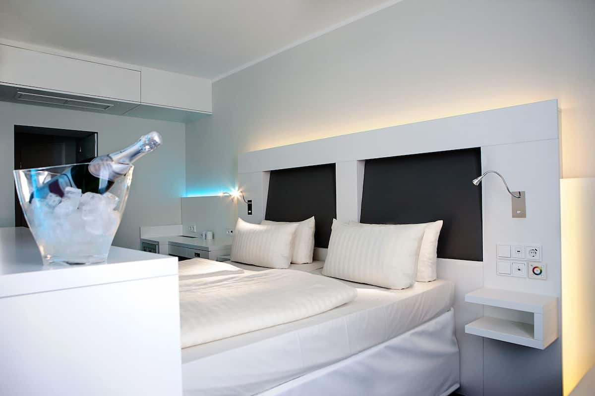 Een moderne hotelkamer met een groot bed, nachtkastjes en een minibar met een fles champagne.
