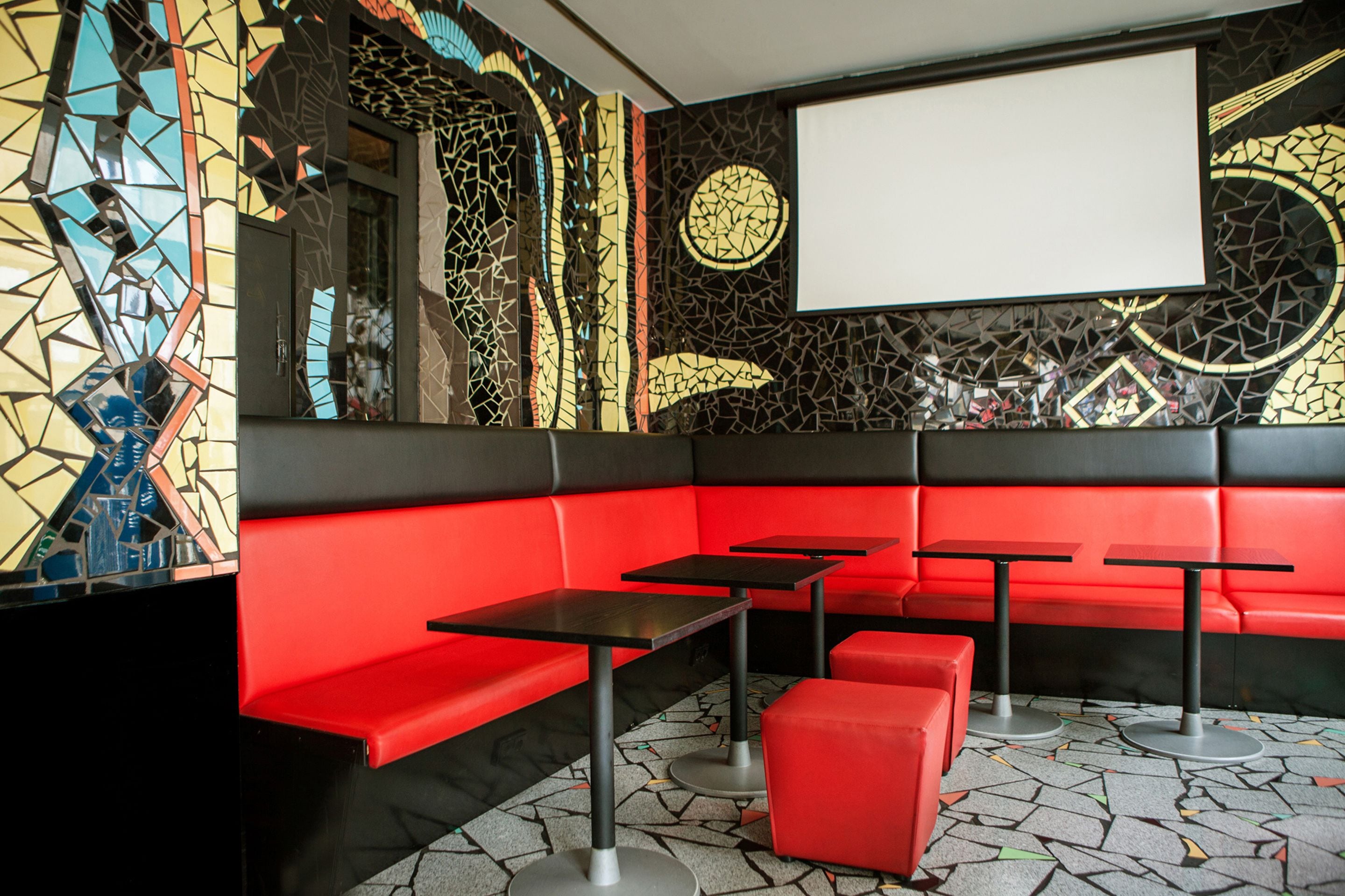 A modern interior with red seating, black tables, and a mosaic wall.