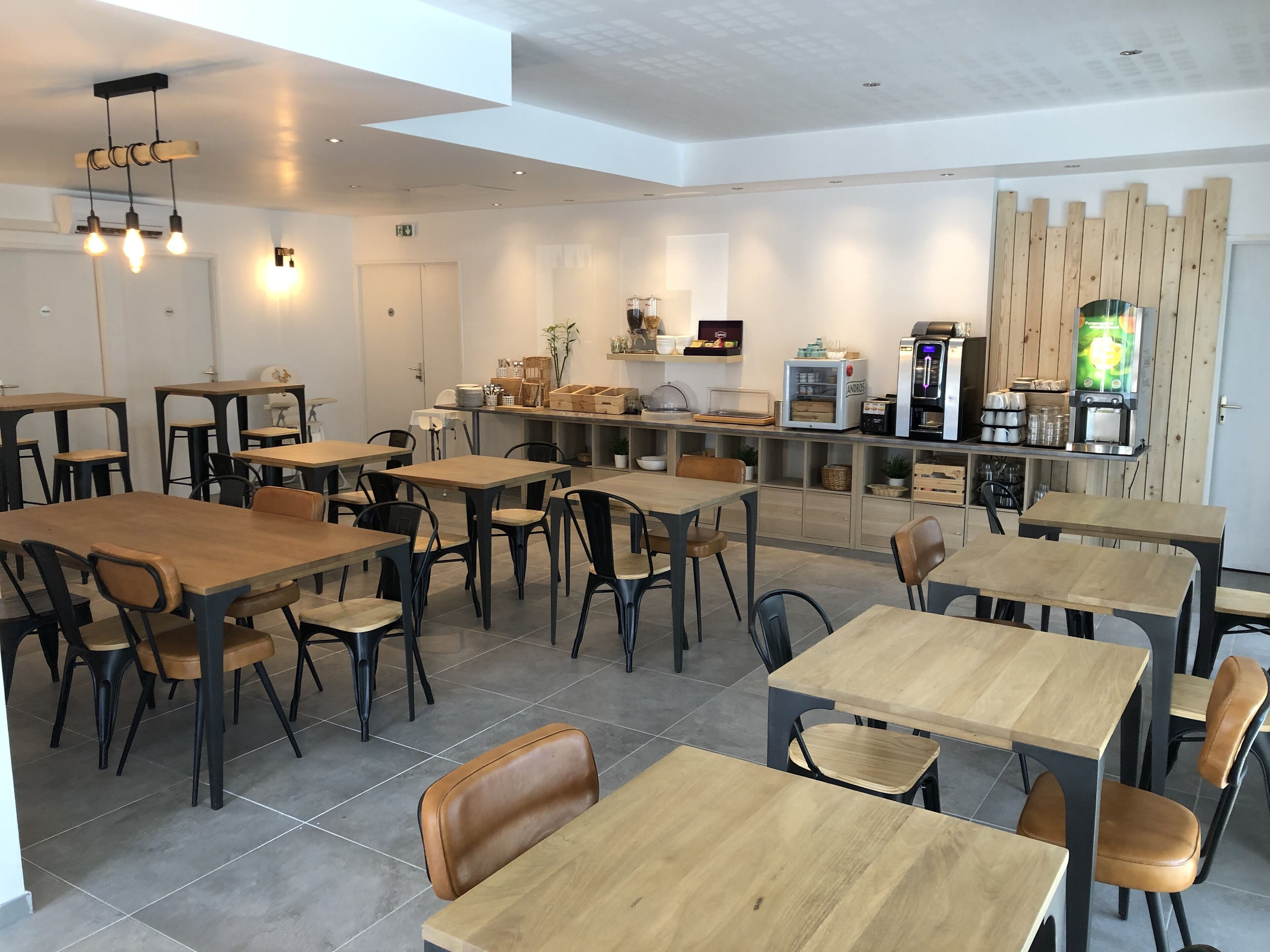 A modern cafe with wooden tables and chairs, a coffee machine, and a wooden partition wall.