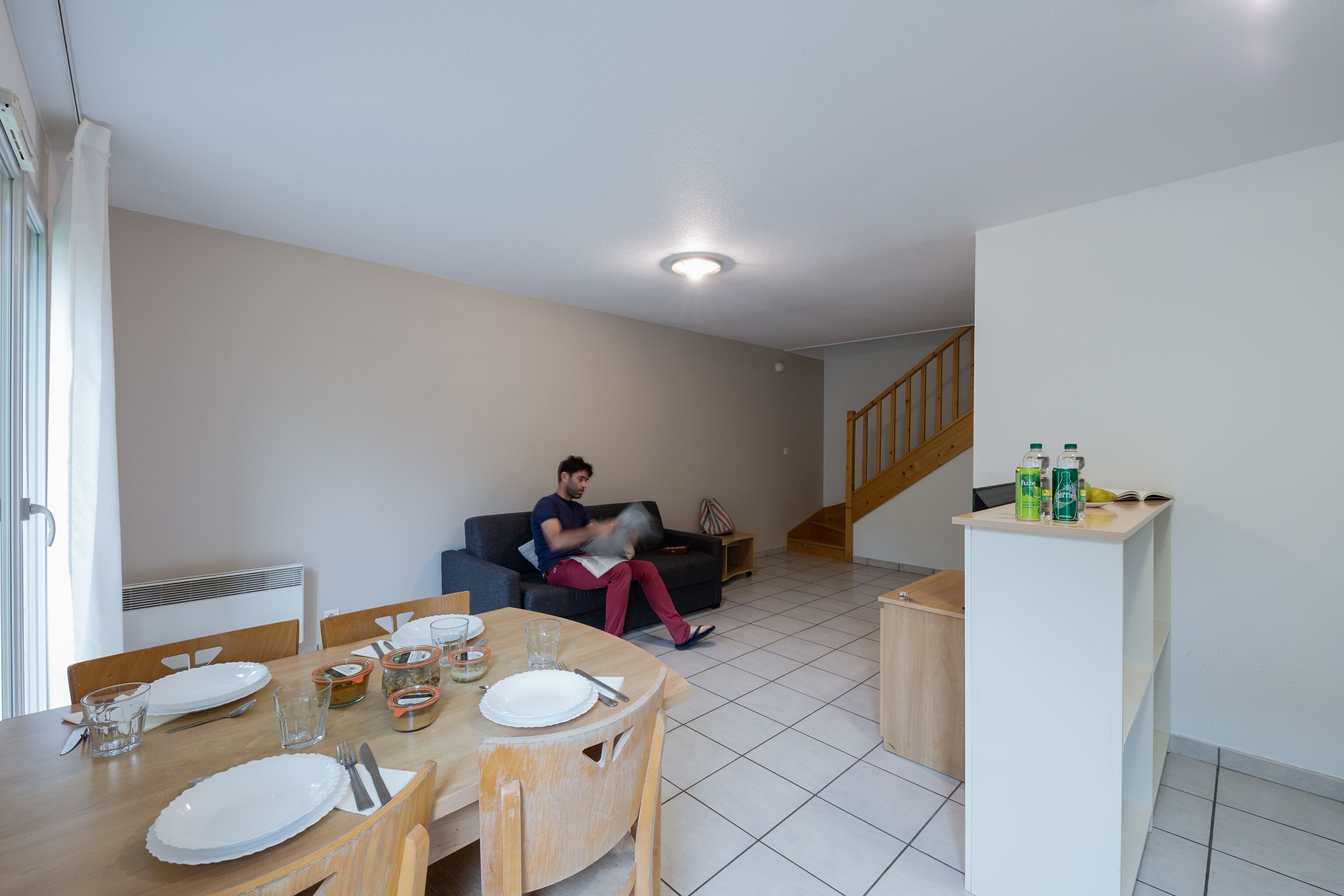 Un salon avec une table à manger dressée pour quatre personnes, un canapé et une personne assise sur le canapé.