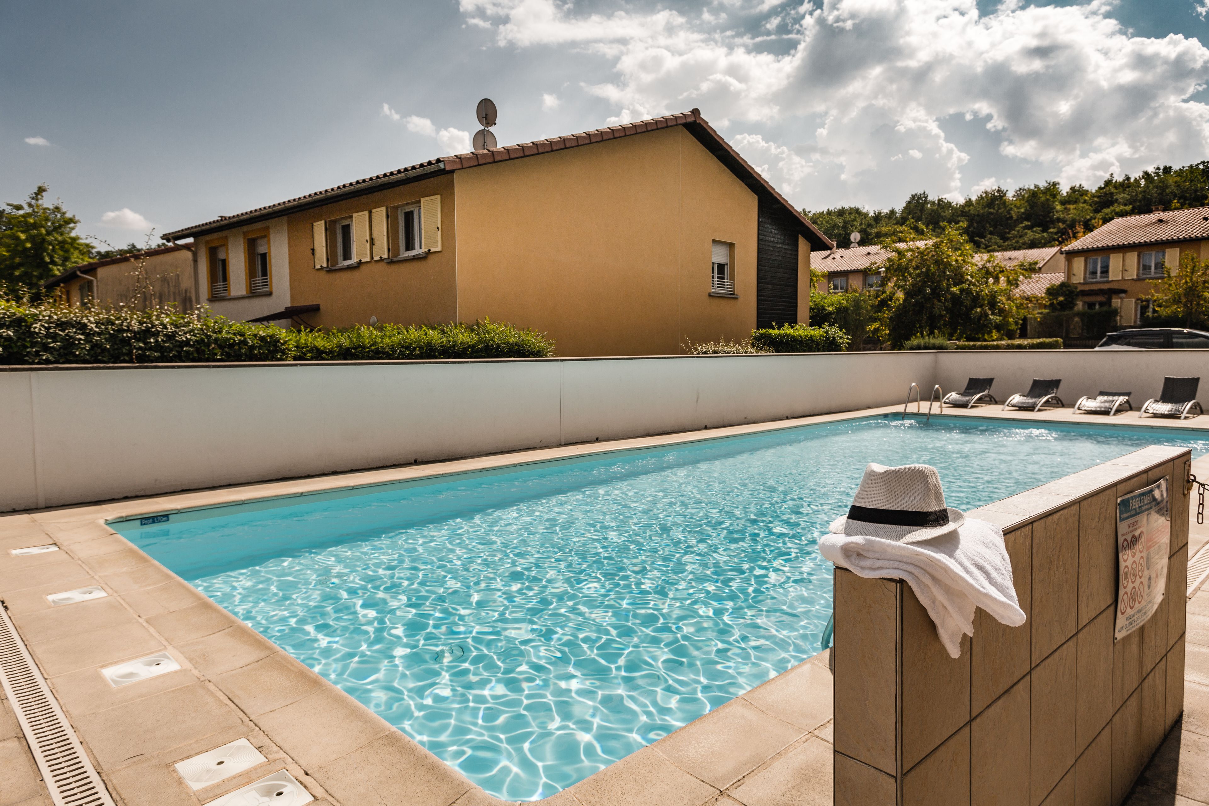 Une piscine avec une terrasse carrelée, un porte-serviettes et une maison en arrière-plan.